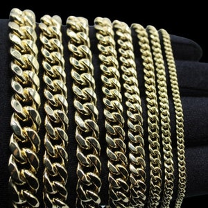 May include: A set of gold chains of varying widths and lengths. The chains are arranged in a row on a black surface.