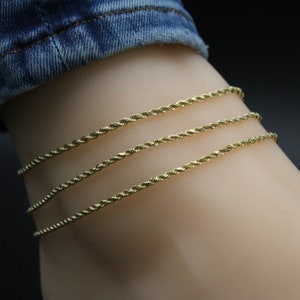 May include: Three gold rope chain anklets layered on a model's ankle.