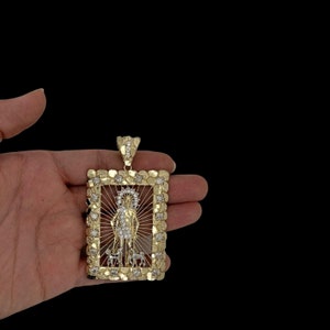 May include: A gold pendant with a square frame featuring a religious figure with a halo and two dogs. The frame is decorated with small, round stones.