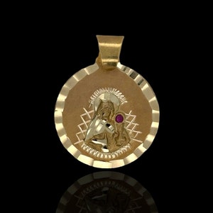 Puede incluir: Pendiente de oro con una imagen detallada de la Virgen María y el niño Jesús. El pendiente tiene un acento de piedra preciosa roja y un borde festoneado.