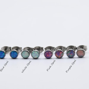 May include: A collection of round stud earrings with various opal colors, including blue, white, pink, and purple. Each earring has a silver-colored post. The names of the colors are written below each pair of earrings.