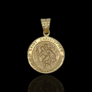 Op de afbeelding: Gouden hanger met de heilige Christoffel die een kind draagt. De hanger is rond en heeft de woorden "Heilige Christoffel Bescherm ons" rond de rand.