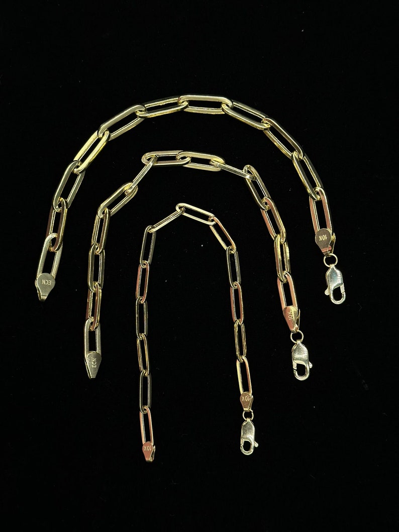 May include: Three gold chain necklaces with different lengths. The chains are made of oval-shaped links. The chains have lobster claw clasps.