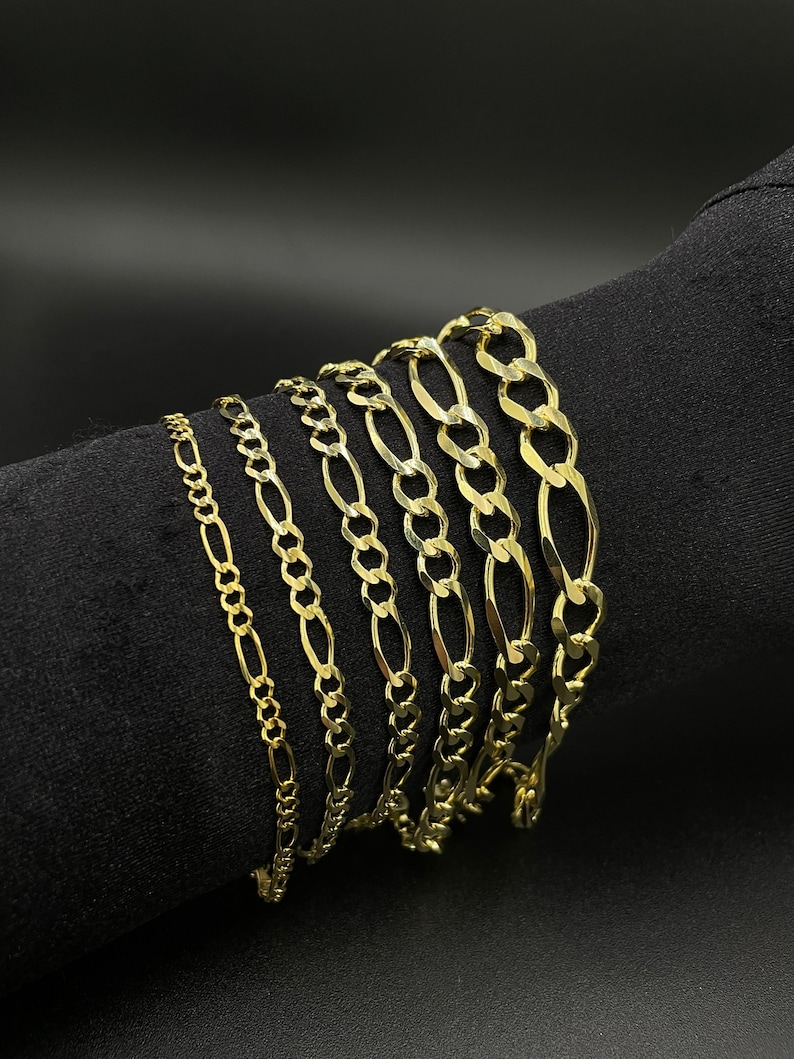 May include: A set of seven gold chain bracelets of varying widths and lengths. The chains are all made of a classic, flat, oval-shaped link.