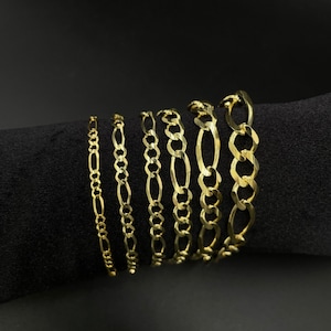 May include: A set of seven gold chain bracelets of varying widths, displayed on a black fabric background.