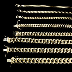 May include: Six gold chains of varying lengths and thicknesses, all with a curb link design. The chains are laid out horizontally on a black background.