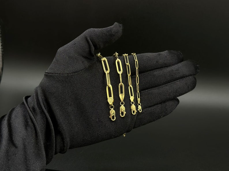May include: Five gold chain necklaces with different lengths and link styles. The chains are displayed on a black fabric background.
