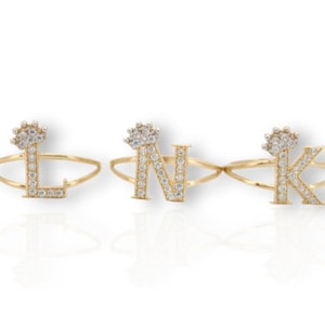 以下が含まれることがあります： L、N、Kの文字が刻まれた3つの金のリング。クリアなキュービックジルコニアがセットされています。各リングには、王冠の形をしたトップがあります。