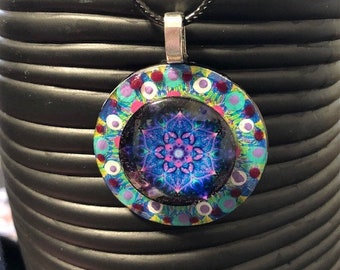 May include: A black cord necklace with a round pendant featuring a colorful mandala design. The mandala has a blue, purple, and pink center with green, white, and red accents.