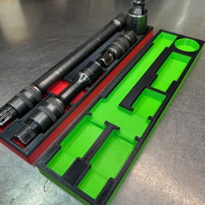 May include: A set of black metal tools in a red and green organizer. The organizer has a black border and is divided into sections to hold the tools. The tools are various sizes and shapes, including sockets and extensions. The organizer is designed to keep tools organized.