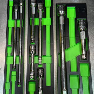 May include: Three sets of mechanic's sockets and extensions in black and green organizers. The sockets and extensions are silver. The organizers are black with green inserts. The right-most organizer has the number "1/2" printed on it.