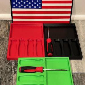 May include: A set of red, black, and green screwdriver organizers with an American flag design. Each organizer holds screwdrivers. The red and black organizers have four slots, while the green one has three. The flag is red, white, and blue.