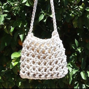 May include: A white crocheted tote bag with a thick rope handle. The bag is hanging from a tree branch.