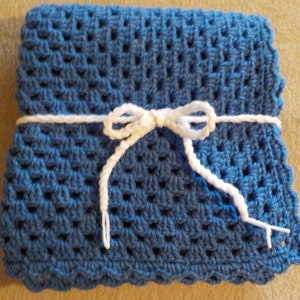 Peut inclure: Une couverture pour b&eacute;b&eacute; en crochet bleu, nou&eacute;e avec un ruban blanc. La couverture a un bord festonn&eacute;.