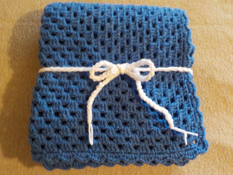 Peut inclure: Une couverture pour b&eacute;b&eacute; en crochet bleu, nou&eacute;e avec un ruban blanc. La couverture a un bord festonn&eacute;.