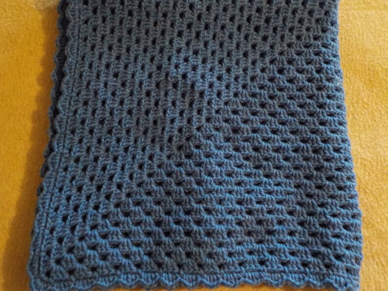 Peut inclure: Une couverture en crochet bleue avec un bord festonn&eacute;. La couverture est r&eacute;alis&eacute;e avec un motif de points textur&eacute;s.