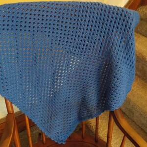 Peut inclure: Une couverture en crochet bleue avec un motif carr&eacute;. La couverture est drap&eacute; sur une chaise en bois.