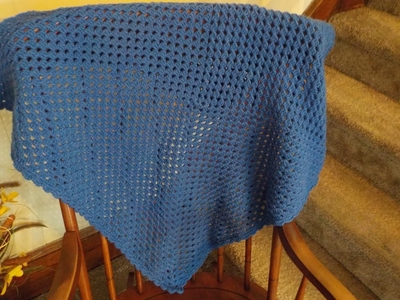 Peut inclure: Une couverture en crochet bleue avec un motif carr&eacute;. La couverture est drap&eacute; sur une chaise en bois.