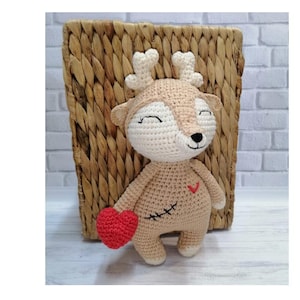 May include: A crocheted deer plush toy holding a red heart. The deer has a stitched-on heart on its chest and a smiling face.
