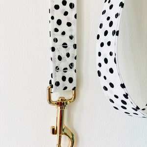 May include: A white and black polka dot dog leash with a gold metal clasp.