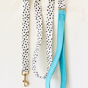 May include: A white and black polka dot dog leash with a solid blue handle. The leash has a gold metal clip.