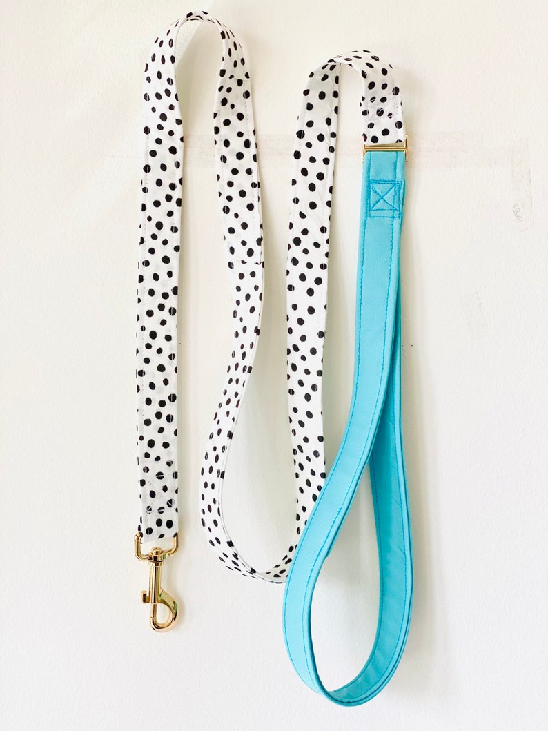 May include: A white and black polka dot dog leash with a solid blue handle. The leash has a gold metal clip.