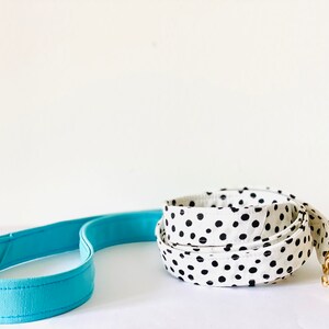 May include: Two dog leashes, one is blue and the other is white with black polka dots. The polka dot leash has a gold metal clip.