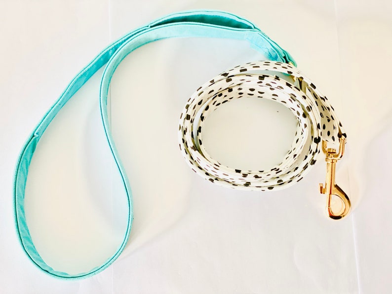 May include: A white and black polka dot dog leash with a light blue handle and a gold metal clasp.