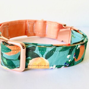 May include: A dog collar featuring a teal fabric with an orange and leaf pattern. The collar has a peach-coloured lining and rose gold hardware, including a buckle and adjuster.