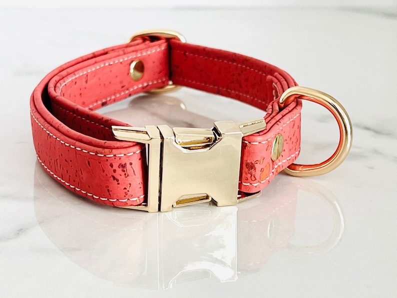 May include: A coral pink cork dog collar with a gold metal buckle and D-ring.