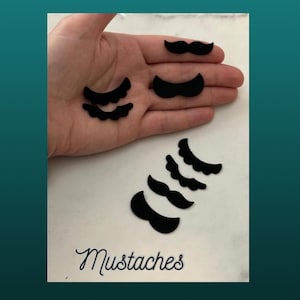 Peut inclure: Un ensemble de formes de moustache en feutre noir, comprenant une moustache traditionnelle et plusieurs styles de moustaches à guidon. Les moustaches sont disposées sur une surface blanche avec le mot "Mustaches" écrit en dessous.