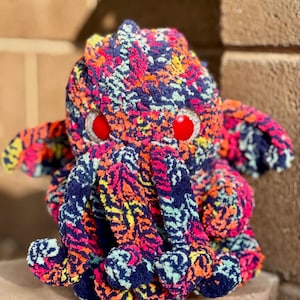 Può includere: Un colorato pupazzo di Cthulhu in peluche dai colori neon vibranti. La bambola presenta occhi rossi, molteplici tentacoli e un design strutturato e fantasia. Il peluche è realizzato in materiale morbido ed è adatto all'esposizione o al gioco.