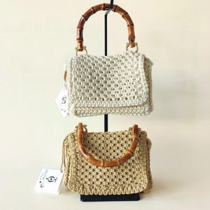 May include: Two crocheted handbags with bamboo handles. The top bag is white and the bottom bag is brown.