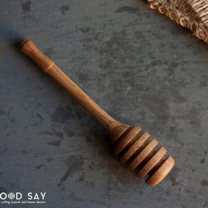 May include: A wooden honey dipper with a long handle and a spiral design. The dipper is made of light brown wood and has a natural finish.