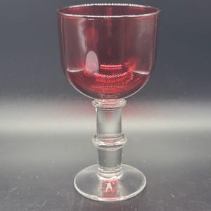 Peut inclure: Un verre à vin transparent rempli d'un liquide rouge rubis. Le verre a une coupe arrondie, un pied avec un design cylindrique et une base circulaire. Le verre est probablement en cristal ou dans un matériau similaire.