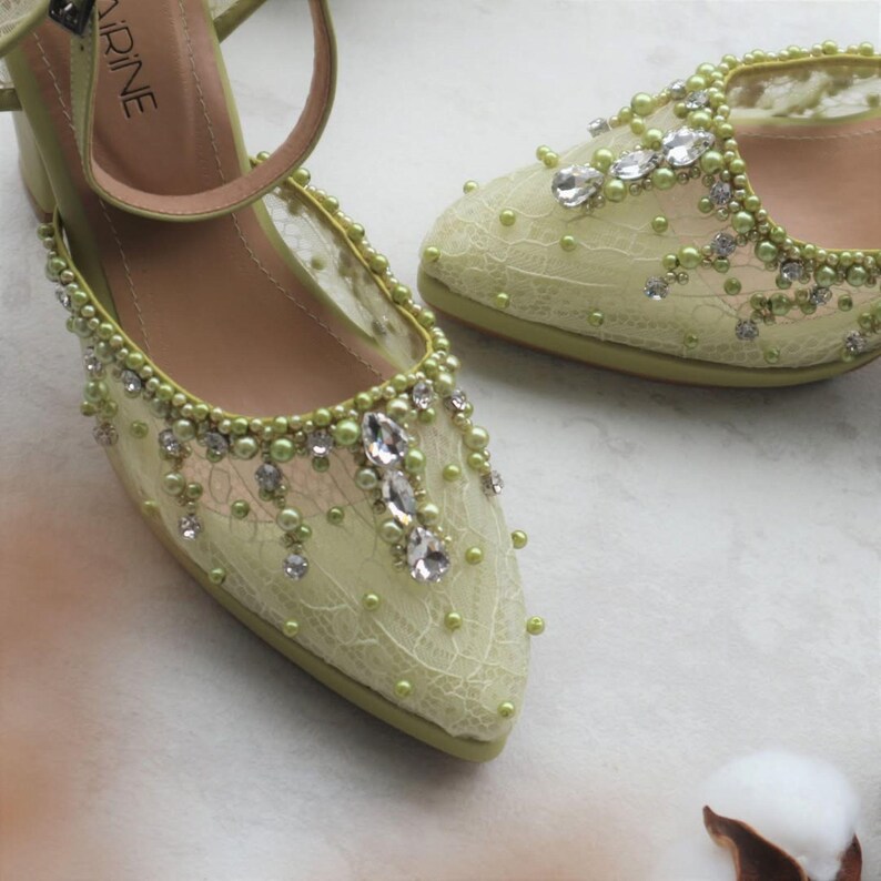 May include: A pair of light green bridal shoes with delicate lace detailing and embellishments. The shoes feature a pointed toe and a small heel. The embellishments include pearls, rhinestones, and crystals.