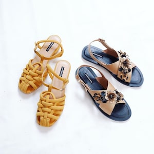 K&ouml;nnte beinhalten: Zwei Paar Sandalen. Ein Paar ist gelb mit einem gewebten Design. Das andere Paar ist braun mit einer schwarzen Sohle und mit goldenen Blumen verziert.