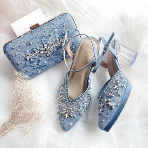以下が含まれることがあります： クリアなアクリルヒールと、それに合わせたライトブルーのサテン素材のクラッチバッグが付いた、ライトブルーのサテン素材のハイヒール。靴とクラッチバッグの両方に、ラインストーンとパールがあしらわれています。
