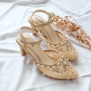 May include: A pair of beige high-heeled shoes with a mesh upper and pearl and rhinestone embellishments. The shoes have a delicate ankle strap with a buckle closure. The brand name "CELLINE" is visible on the insole.
