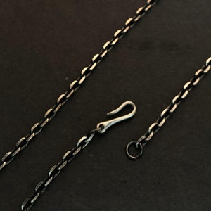 Könnte beinhalten: Eine silberne Kettenkette mit einem Karabinerverschluss und einem Sprungring. Die Kette besteht aus kleinen, ovalen Gliedern.