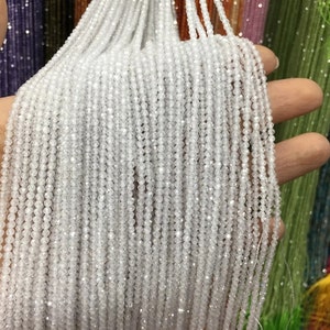 May include: A close-up of a strand of white faceted crystal beads. The beads are small and round, and they are strung on a thin wire. The beads are very shiny and reflect light.
