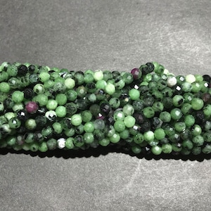 May include: A strand of green, black, and pink gemstone beads. The beads are round and faceted.