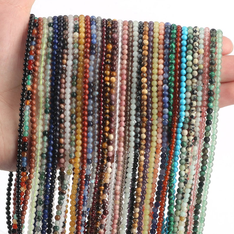 May include: A collection of 40 strands of various gemstone beads, each strand is approximately 16 inches long. The beads are round and come in a variety of colors, including green, blue, red, brown, and white.