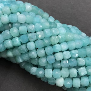 May include: A strand of light blue aquamarine beads, each bead is faceted and has a square shape.
