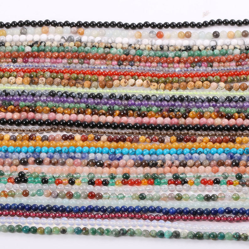 May include: Assortment of colorful gemstone beads, including amethyst, turquoise, carnelian, and agate. The beads are strung on a white background.