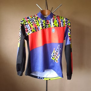 Pode incluir: Uma camisola de ciclismo de manga comprida com uma estampa abstrata colorida. A camisola tem um padrão preto, vermelho, azul e verde com um zíper branco.