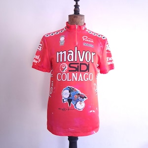 Könnte beinhalten: Ein rotes Vintage-Radtrikot mit den Logos "malvor" und "colango". Das Trikot hat einen Halb-Reißverschluss-Kragen und kurze Ärmel. Es zeigt auch eine farbenfrohe Grafik eines Fahrrads und das Jahr 1989.