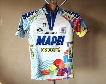 May include: White cycling jersey with a blue zipper and colorful geometric pattern. The jersey has the logos "Mapei", "Bricobi", "Latexco", and "Sportful".