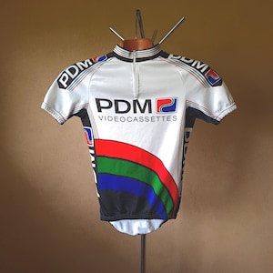 May include: White cycling jersey with a black, red, blue and green stripe design. The jersey has a zip and the text "PDM VIDEOCASSETTES" on the front.