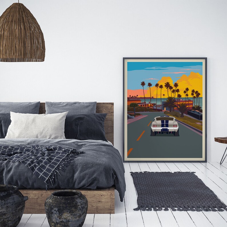 K&ouml;nnte beinhalten: Ein gerahmtes Poster mit einer Retro-Illustration eines wei&szlig;en Autos, das eine von Palmen ges&auml;umte Stra&szlig;e entlangf&auml;hrt. Der Himmel ist ein leuchtend orangefarbener und gelber Sonnenuntergang. Das Poster h&auml;ngt an einer wei&szlig;en Wand in einem Raum mit einem Bett und einer Korblampen.